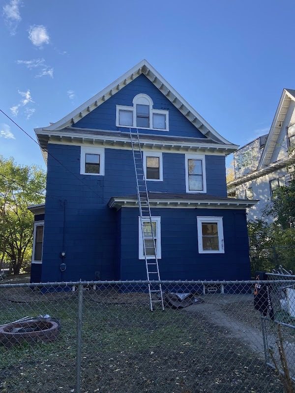 Two-and-a-half story home freshly repainted deep navy with white window trim and an extension ladder against the gable