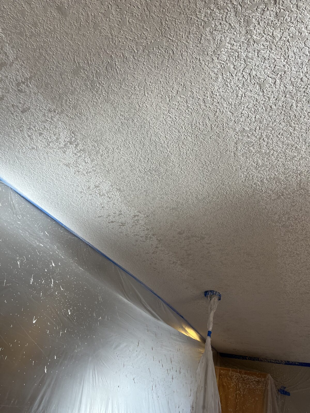 Repaired ceiling with knockdown texture blended seamlessly into the surrounding original texture, room masked off with plastic